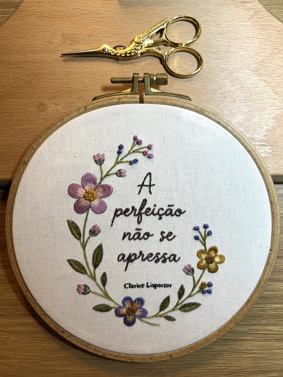 Bastidor com bordado de flores e a frase “A perfeição não se apressa”, de Clarice Lispector